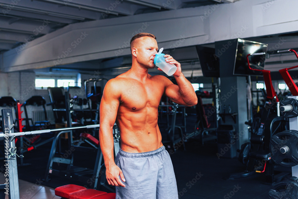 Young caucasian man drinking water after exercise.man in the gym drinking from the shaker.Toned. Young caucasian man drinking water after exercise.man in the gym drinking from the shaker.Toned.