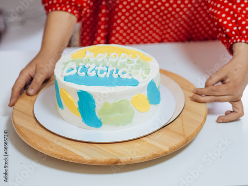 white birthday homemade cake on a wooden stand with woman's hands. photo