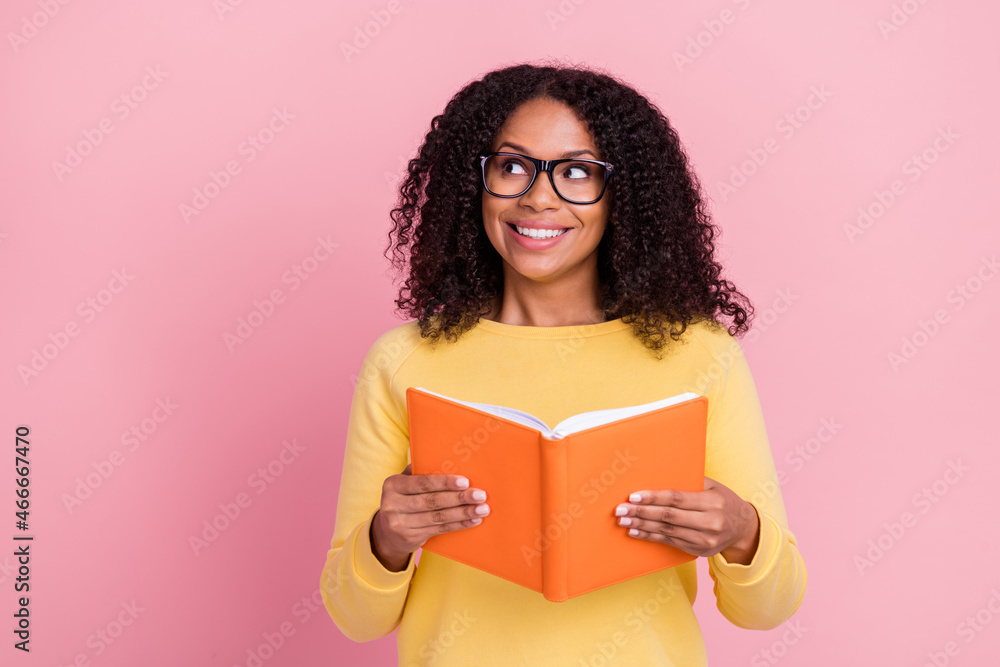 Photo of excited dreamy dark skin girl dressed yellow pullover glasses holding book looking empty space isolated pink color background Photo of excited dreamy dark skin girl dressed yellow pullover glasses holding book looking empty space isolated pink color background