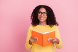 Photo of excited dreamy dark skin girl dressed yellow pullover glasses holding book looking empty space isolated pink color background