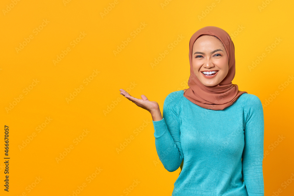 Portrait of smiling young Asian woman showing copy space on palm isolated over yellow background Portrait of smiling young Asian woman showing copy space on palm isolated over yellow background