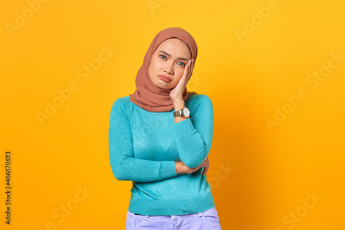 Frustrated young Asian woman holding face with a hand on yellow background © Sewupari Studio