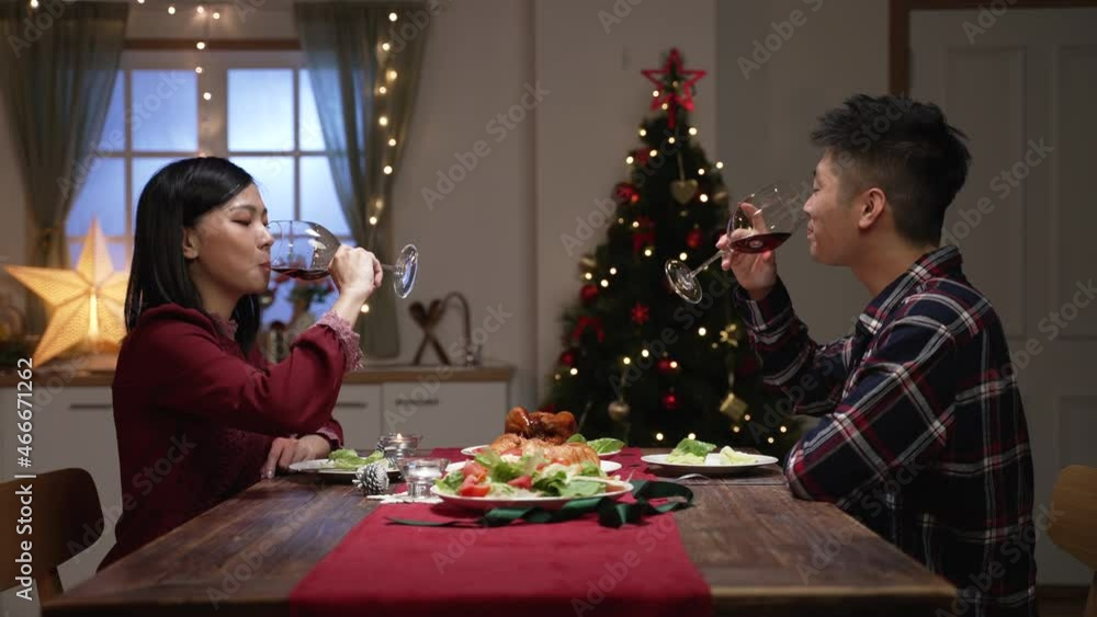 side view loving asian young couple making new year toast while they are chatting and enjoying festive dinner in dining room at home with Christmas decorations side view loving asian young couple making new year toast while they are chatting and enjoying festive dinner in dining room at home with Christmas decorations