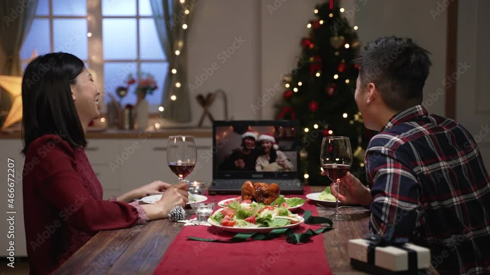 view from behind cheerful asian couple looking at laptop screen while having virtual double dates with friends via video conferencing on Christmas eve at dinner view from behind cheerful asian couple looking at laptop screen while having virtual double dates with friends via video conferencing on Christmas eve at dinner