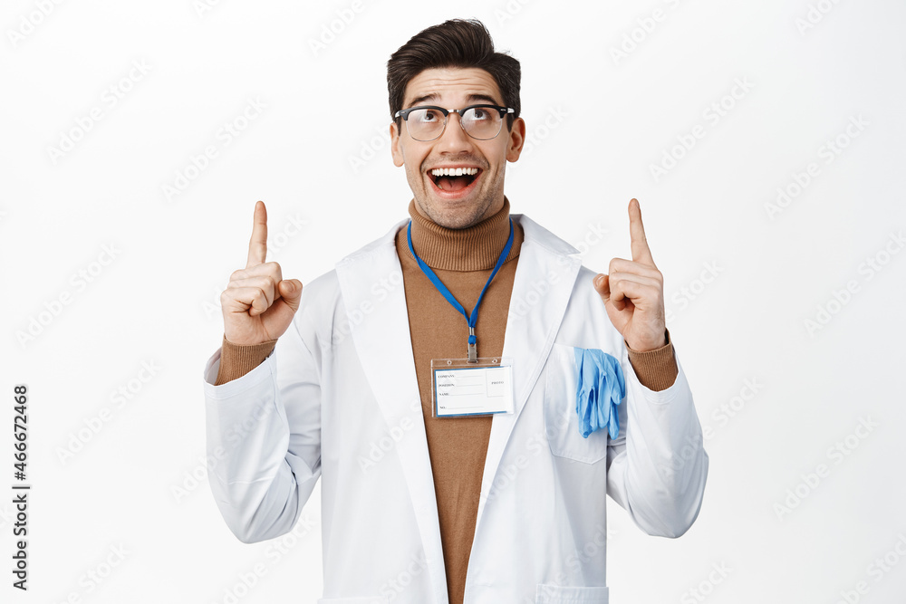Medical personal and healthcare workers. Happy smiling male doctor in glasses and robe, pointing and looking up with excited face, white background Medical personal and healthcare workers. Happy smiling male doctor in glasses and robe, pointing and looking up with excited face, white background