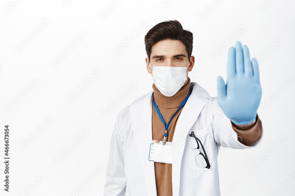 Healthcare worker in face mask from covid 19, wearing rubber gloves, showing stop no gesture, taboo and prohibition sign, standing over white background