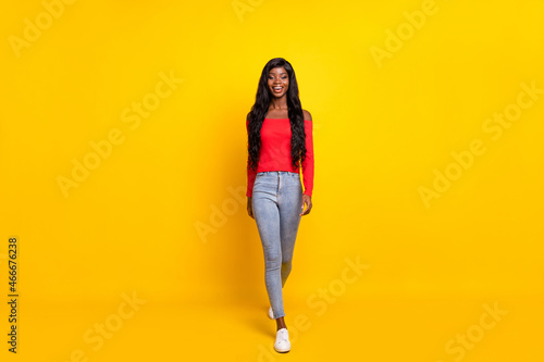 Photo of adorable shiny dark skin girl dressed red top walking isolated yellow color background