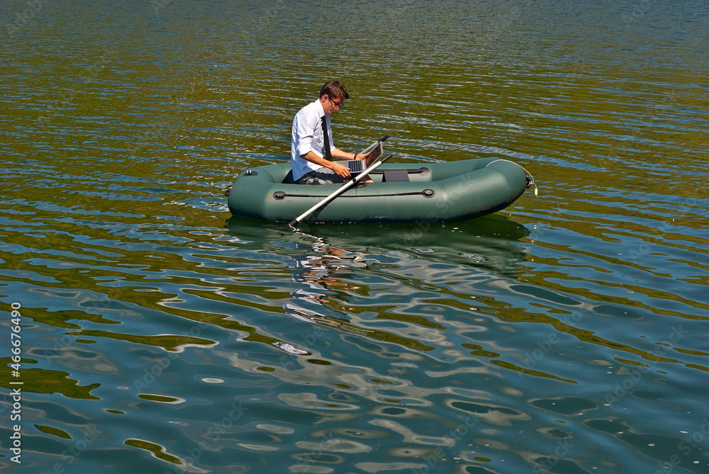 Naklejka premium A man in a white shirt on an inflatable boat. Businessman with laptop resting on the lake. The concept of remote work, leisure and freelance.