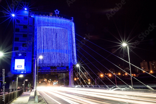 Long exposure photograph showing the bridge tower with blue Christmas lights  and white car headlights.