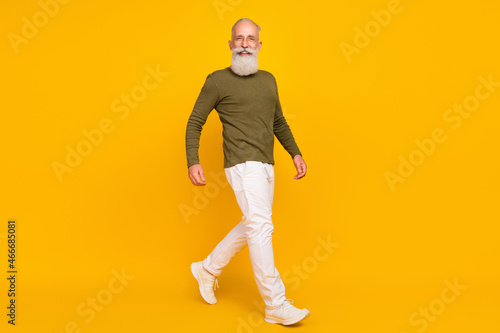 Photo of positive traveler old man walk wear glasses green shirt pants sneakers isolated yellow color background