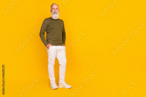 Photo of positive pensioner man posing hands pocket wear green shirt trousers sneakers isolated yellow color background