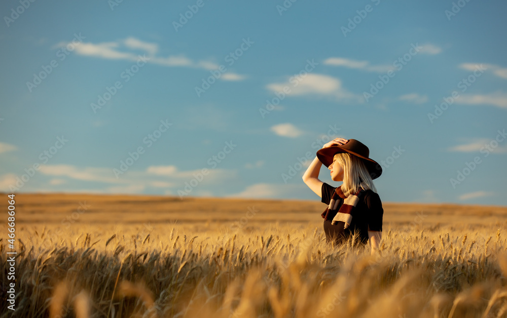 Blonde woman in black dress and hat with scarf in wheat field in autumn season time