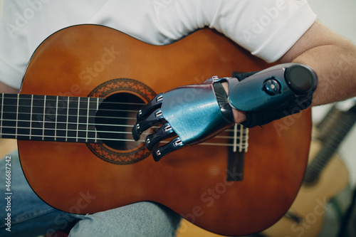 Young disabled man with artificial prosthetic hand plays on guitar strings at shop