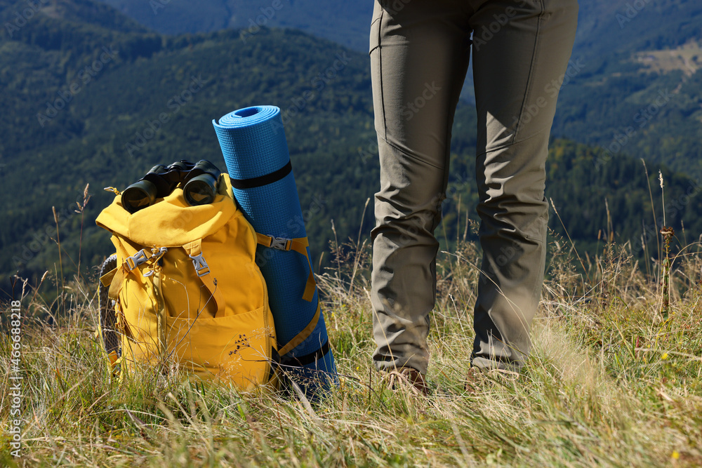 Tourist with backpack, sleeping pad and binoculars in mountains on sunny day, closeup Tourist with backpack, sleeping pad and binoculars in mountains on sunny day, closeup
