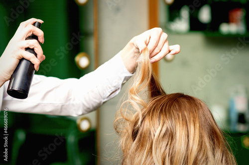Female coiffeur fixing hairstyling of blonde woman with hairspray in a beauty salon photo