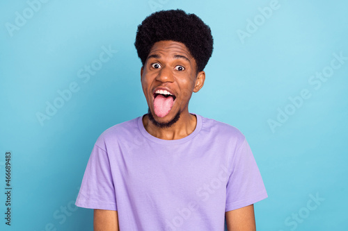 Photo of cool millennial brunet guy tongue out wear violet t-shirt isolated on blue color background