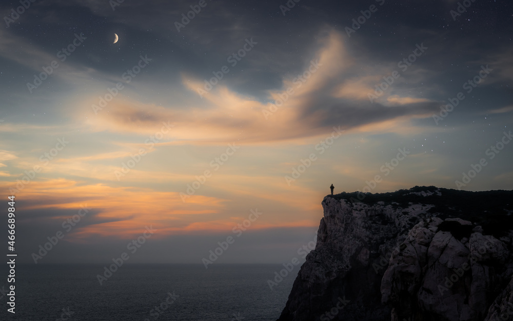 Man watching a beautiful and unique surreal bird-shaped cloud under the starry night sky over the sea at sunset in Sardinia, Italy Man watching a beautiful and unique surreal bird-shaped cloud under the starry night sky over the sea at sunset in Sardinia, Italy