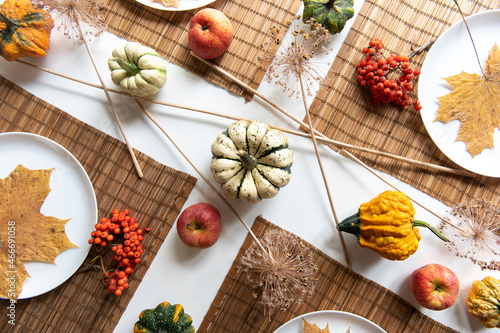 flat lay of small pumpkins and dry brown maple leafs on white plates, autumn dinner table decors