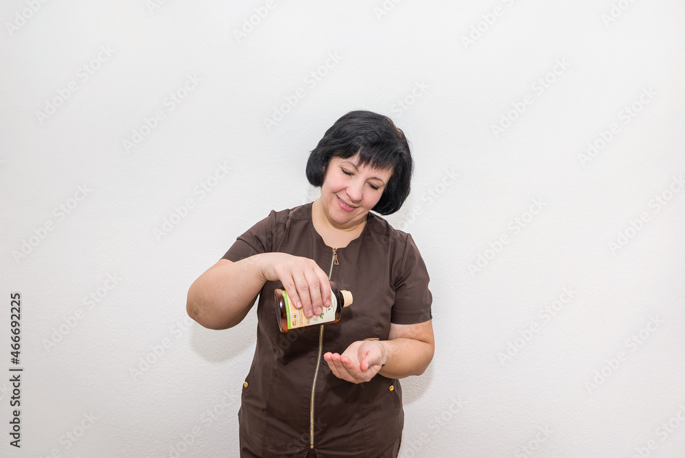 woman in massage parlor pours massage oil on her hand.Portrait of a woman in uniform before a cosmetic procedure woman in massage parlor pours massage oil on her hand.Portrait of a woman in uniform before a cosmetic procedure