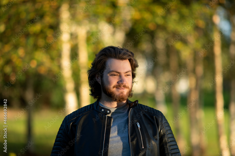 A thoughtful young bearded man smiling against a blurred background of colored autumn leaves A thoughtful young bearded man smiling against a blurred background of colored autumn leaves