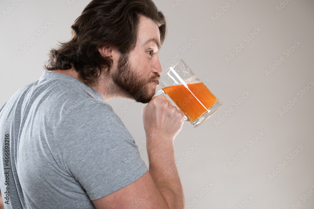 funny bearded man drinking beer with a big mug on a gray background