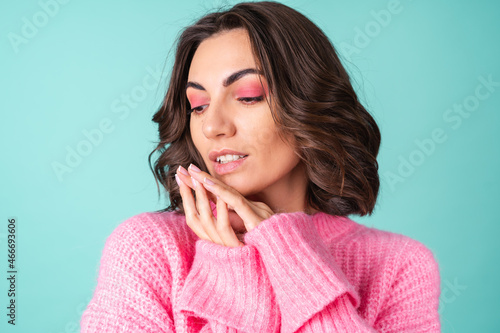 Cozy portrait of a young woman in a pink knitted sweater and with bright makeup on a turquoise background