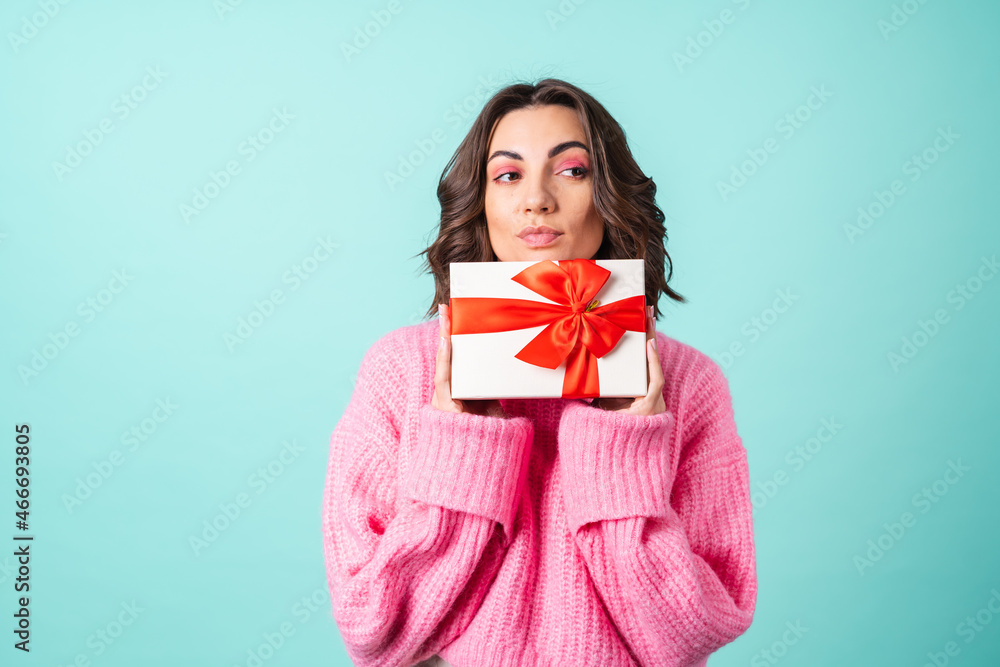 Cozy portrait of a young woman in a pink knitted sweater and with bright makeup on a turquoise background with a gift box with a red bow Cozy portrait of a young woman in a pink knitted sweater and with bright makeup on a turquoise background with a gift box with a red bow
