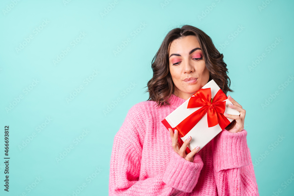 Cozy portrait of a young woman in a pink knitted sweater and with bright makeup on a turquoise background with a gift box with a red bow Cozy portrait of a young woman in a pink knitted sweater and with bright makeup on a turquoise background with a gift box with a red bow