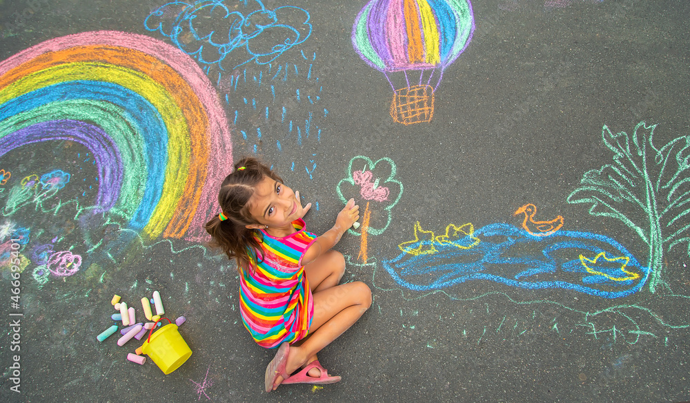 The child draws with chalk on the asphalt. Selective focus. - obrazy, fototapety, plakaty 
