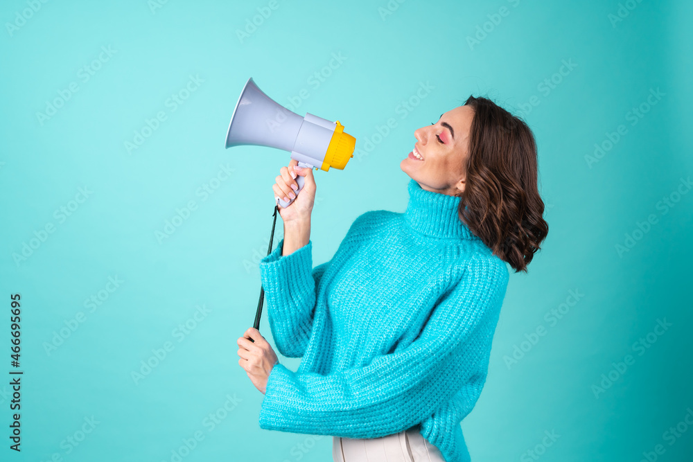 Cozy portrait of a young woman in a knitted blue sweater and bright pink makeup holding a megaphone loudspeaker Cozy portrait of a young woman in a knitted blue sweater and bright pink makeup holding a megaphone loudspeaker