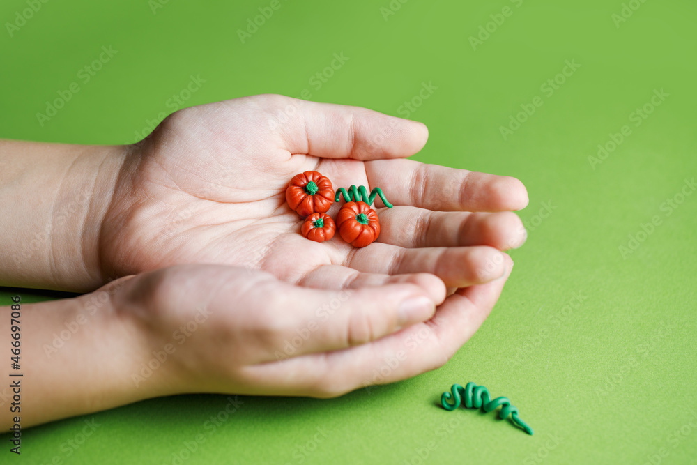 Decorative small pumpkin made of polymer clay in the hand of a child. Miniatures for playing in the dollhouse. Modeling from plasticine by children. Children's creativity. Horizontal photo. Decorative small pumpkin made of polymer clay in the hand of a child. Miniatures for playing in the dollhouse. Modeling from plasticine by children. Children's creativity. Horizontal photo.