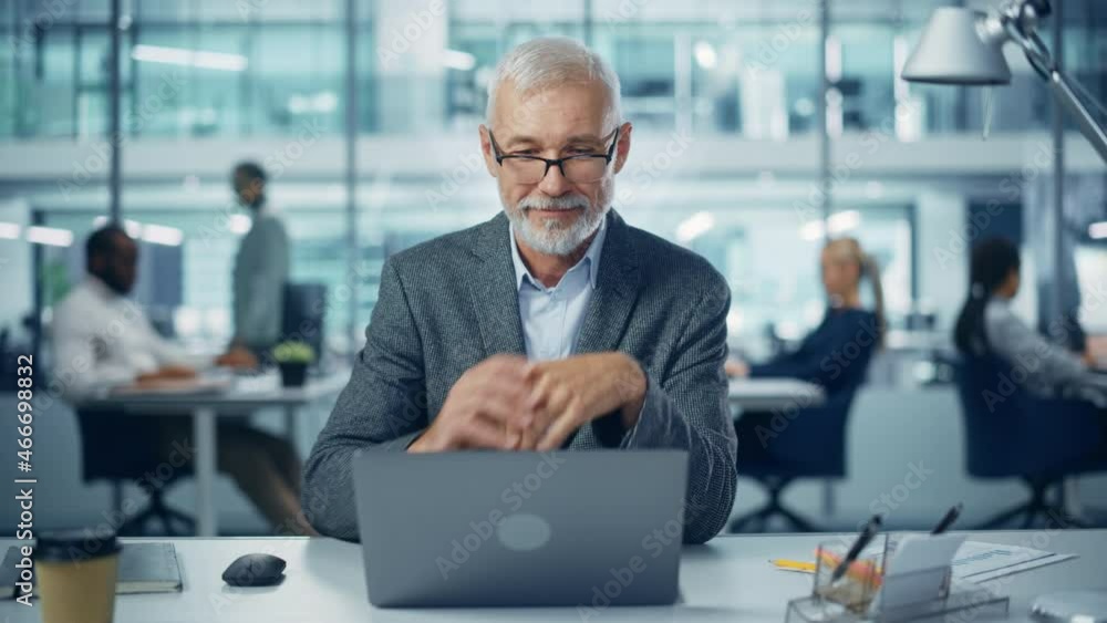 Modern Office: Portrait of Successful Middle Aged Bearded Businessman Working on a Laptop at his Desk. Smiling Corporate Worker. Multi-Ethnic Workplace with Happy Professionals. Front View Static Shot Modern Office: Portrait of Successful Middle Aged Bearded Businessman Working on a Laptop at his Desk. Smiling Corporate Worker. Multi-Ethnic Workplace with Happy Professionals. Front View Static Shot