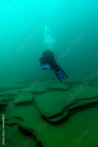 SCUBA diver swimming over large rock plates