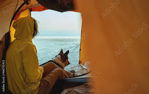 Bilde på lerret Woman and dog are sitting in tourist tent and admiring early morning view at beach