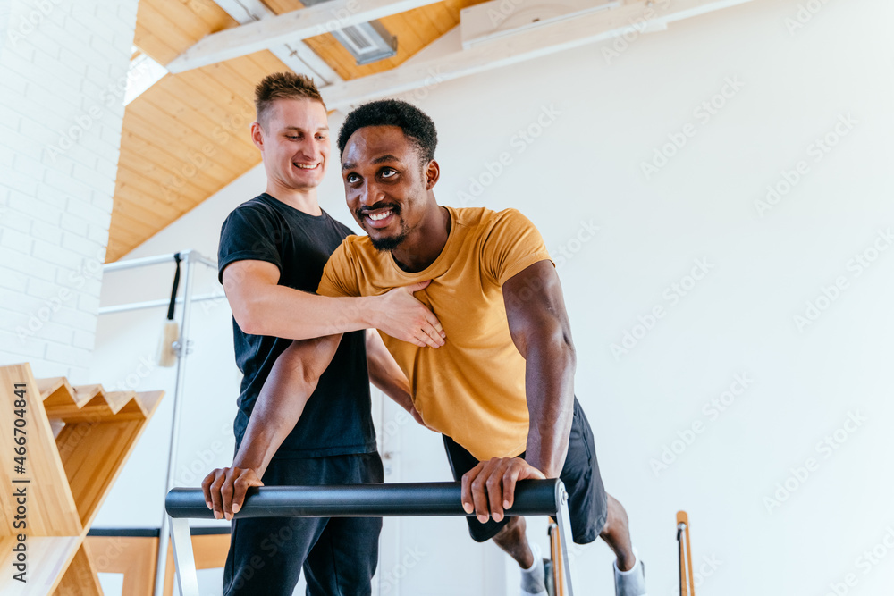 Smiling male coach or instructor help black man client at pilates