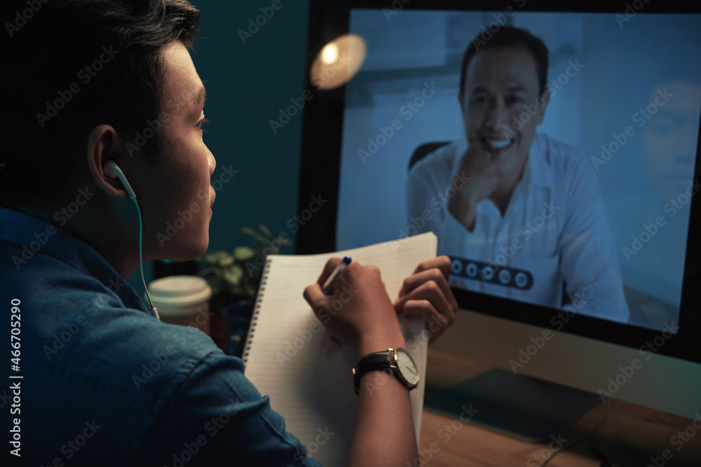 Over shoulder view of Asian student in earphones watching webinar