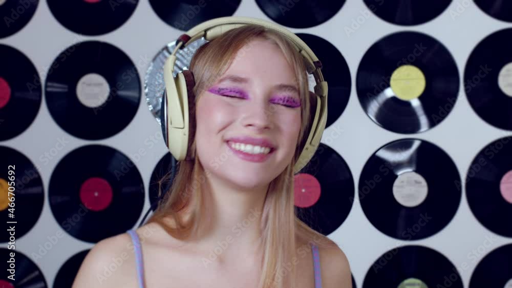 Beautiful girl in headphones sings on vinyl disc wall decoration. Singer, vocalist is recording song for album. Young pop star in musical studio. Female deejay performance. Blonde listening to music Beautiful girl in headphones sings on vinyl disc wall decoration. Singer, vocalist is recording song for album. Young pop star in musical studio. Female deejay performance. Blonde listening to music