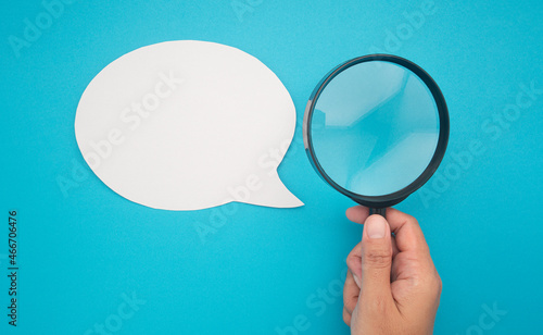 Top view of a blank white speech bubble and hand holding a magnifying glass on a blue background