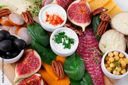 Appetizer assortment with sauces on the wooden board. Cheese, salami, olives, figs, radish, spinach, pecan nuts and fried chickpea. Party food