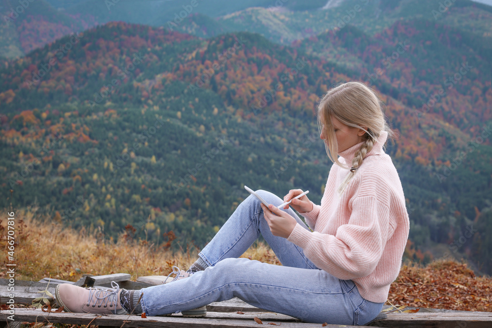 Young woman drawing on tablet in mountains, space for text