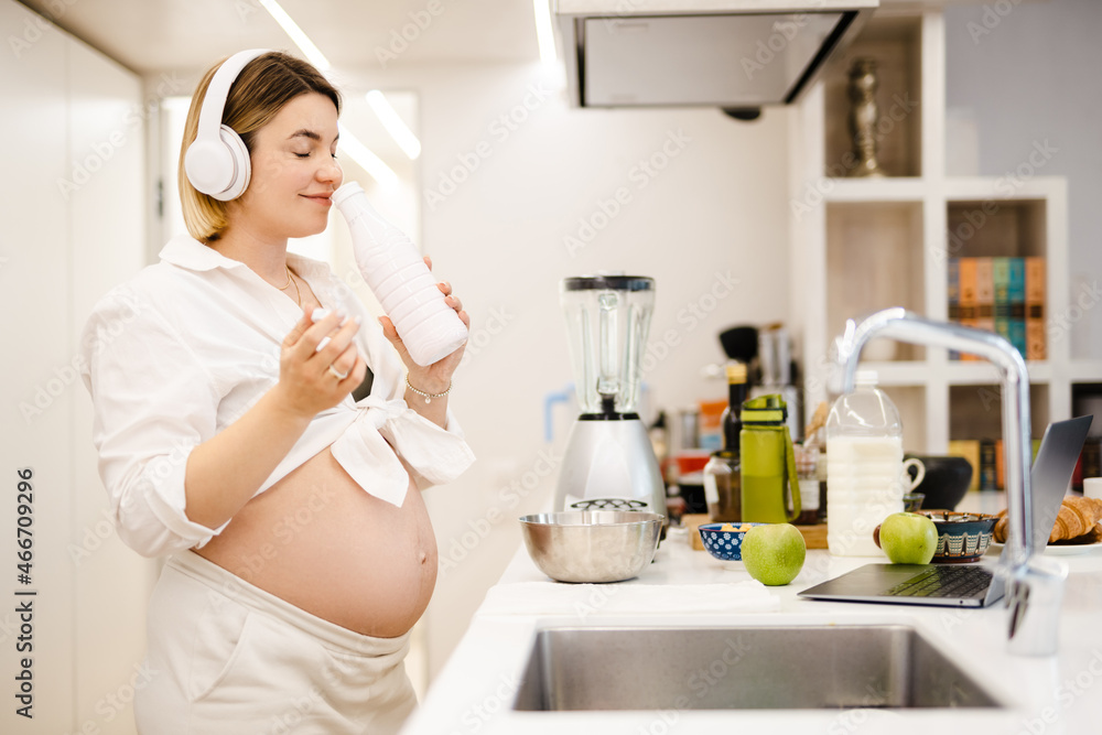 White pregnant woman in headphones making smoothy at home White pregnant woman in headphones making smoothy at home
