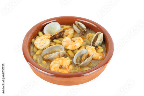 Fabas verdinas with prawns and clams in an earthenware casserole on a white background. Copy space.