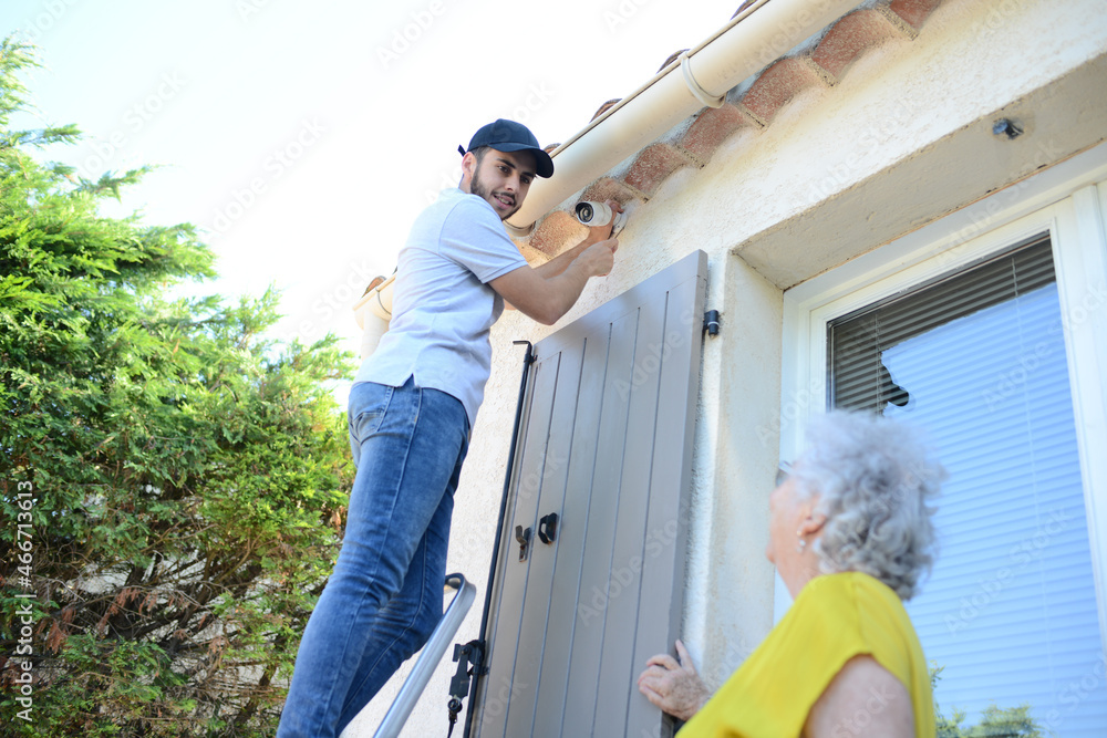 handsome young man installing house security anti burglary camera and siren alarm in a senior woman home