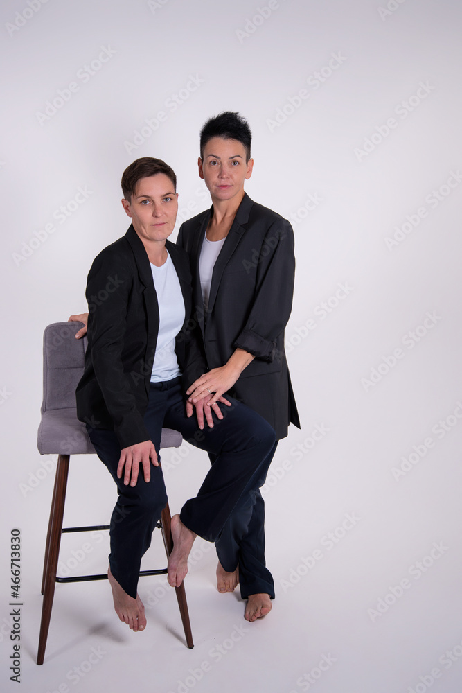 Obraz premium Two pretty women in business suits on a gray background. Girlfriends at the corporate party.