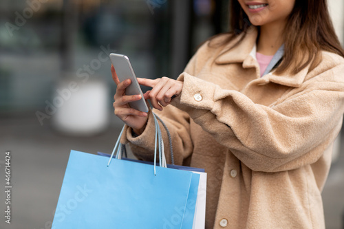 Closeup of young woman using smartphone, holding paper bags, shopping online outdoors