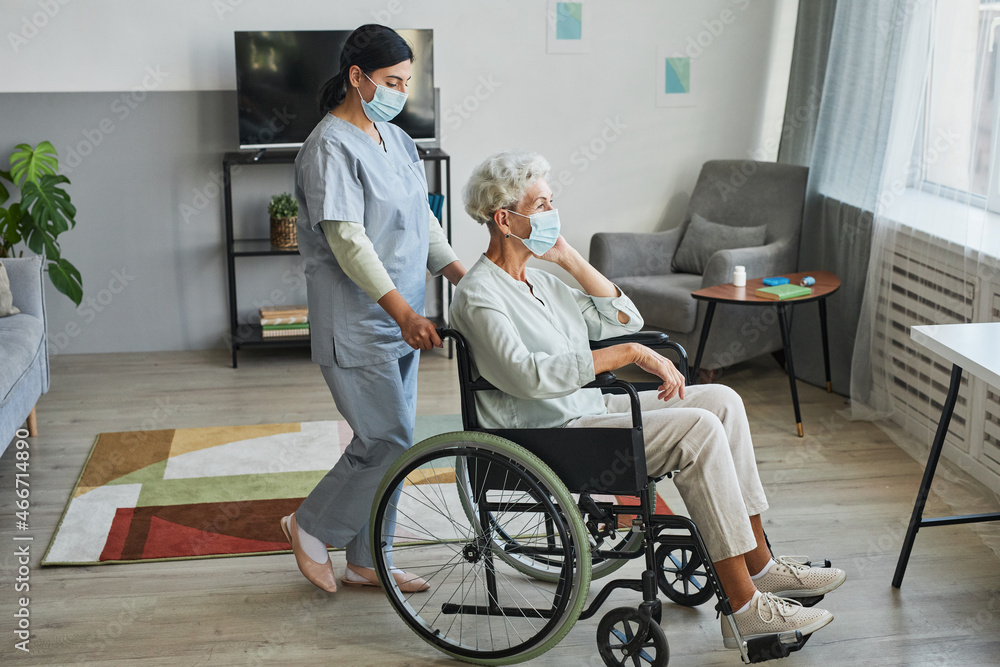 Full length portrait of female nurse assisting senior woman in wheelchair at home or in retirement center, copy space Full length portrait of female nurse assisting senior woman in wheelchair at home or in retirement center, copy space