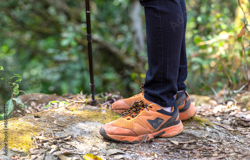 Man wearing trekking shoes, hiker feet standing on the rock in forest. Outdoor adventure concept