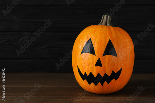 Pumpkin with drawn spooky face on wooden table, space for text. Halloween celebration