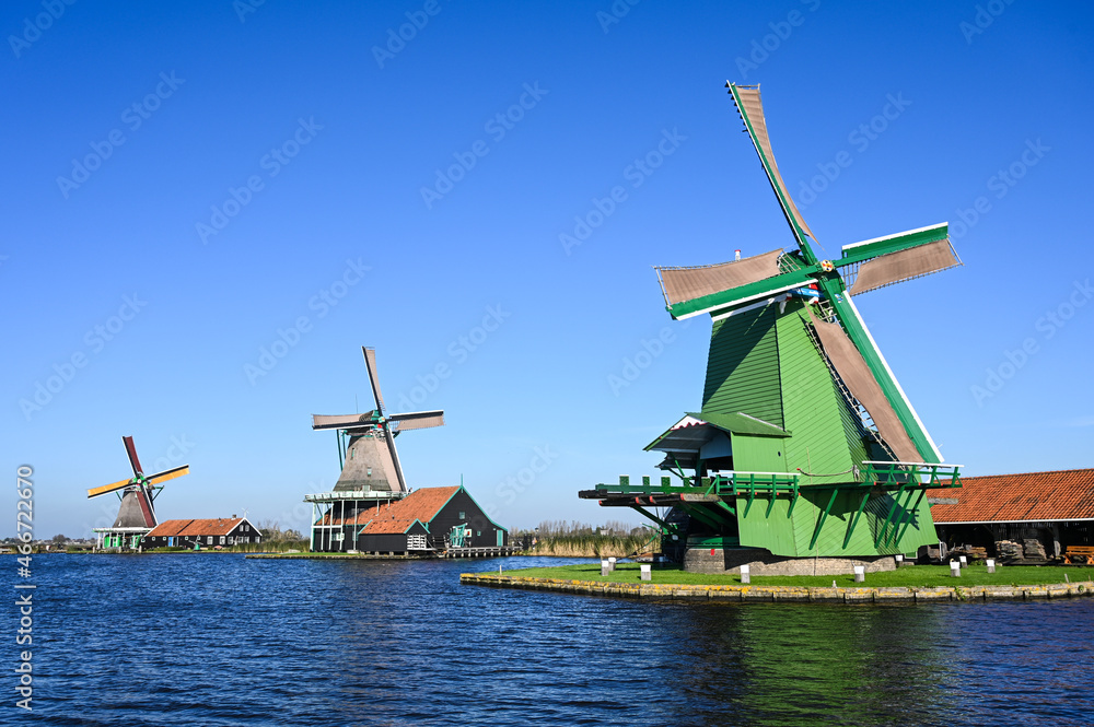 Old windmills by the river in Holland. Traditional Windmill reflected in river canal in Netherlands. Oilmill in Zaanse Schans.