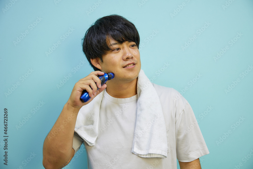白シャツにタオルをかけて髭をそる20代アジア人男性